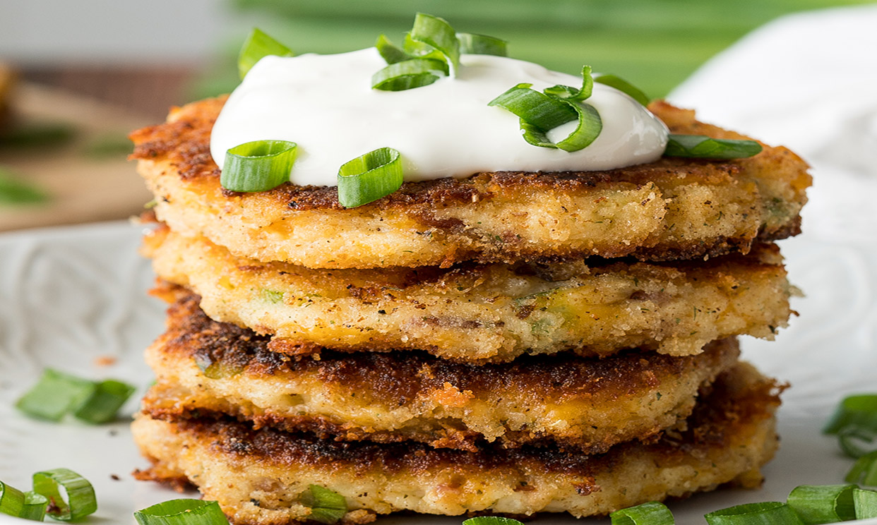 A stack of loaded mashed potato cakes with a dollop of sour cream and green onions