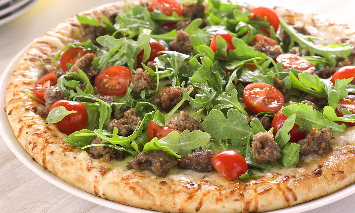 Sausage pizza topped with fresh arugula