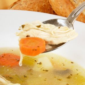 A spoon with chicken and a carrot slice from a bowl of chicken and potato dumpling soup