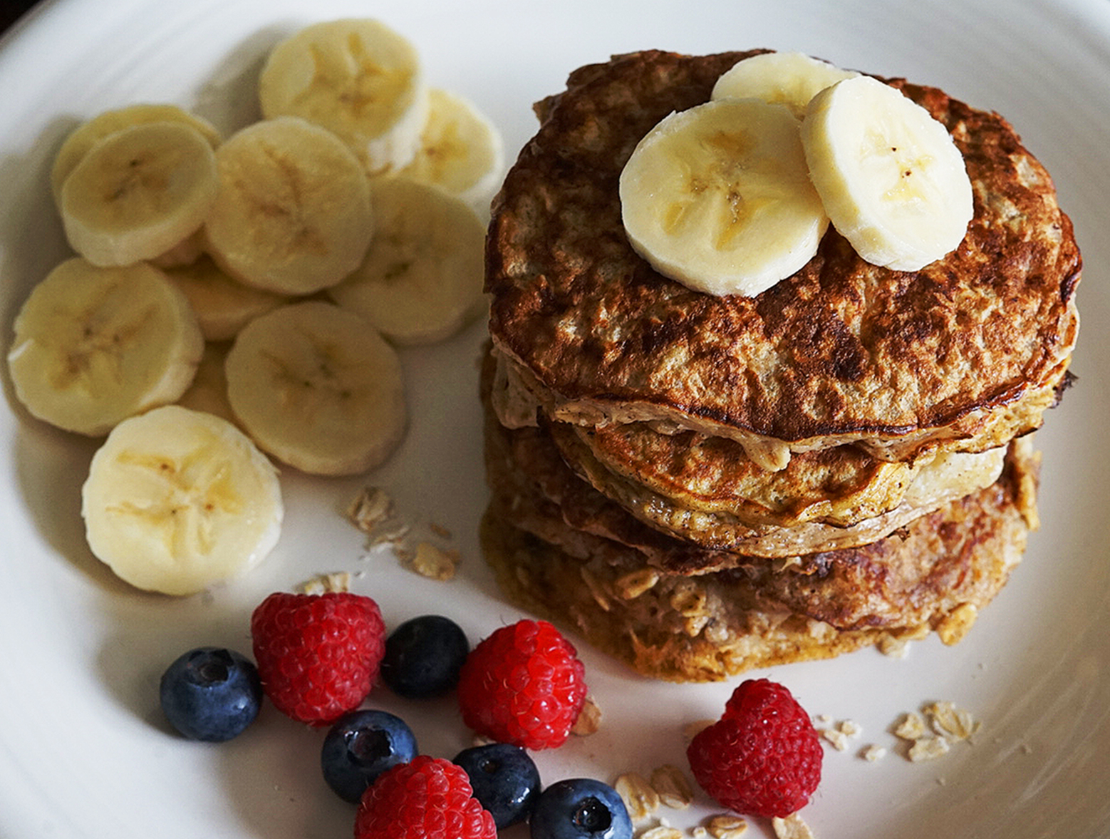 A stack of protein banana pancakes served with banana slices and berries
