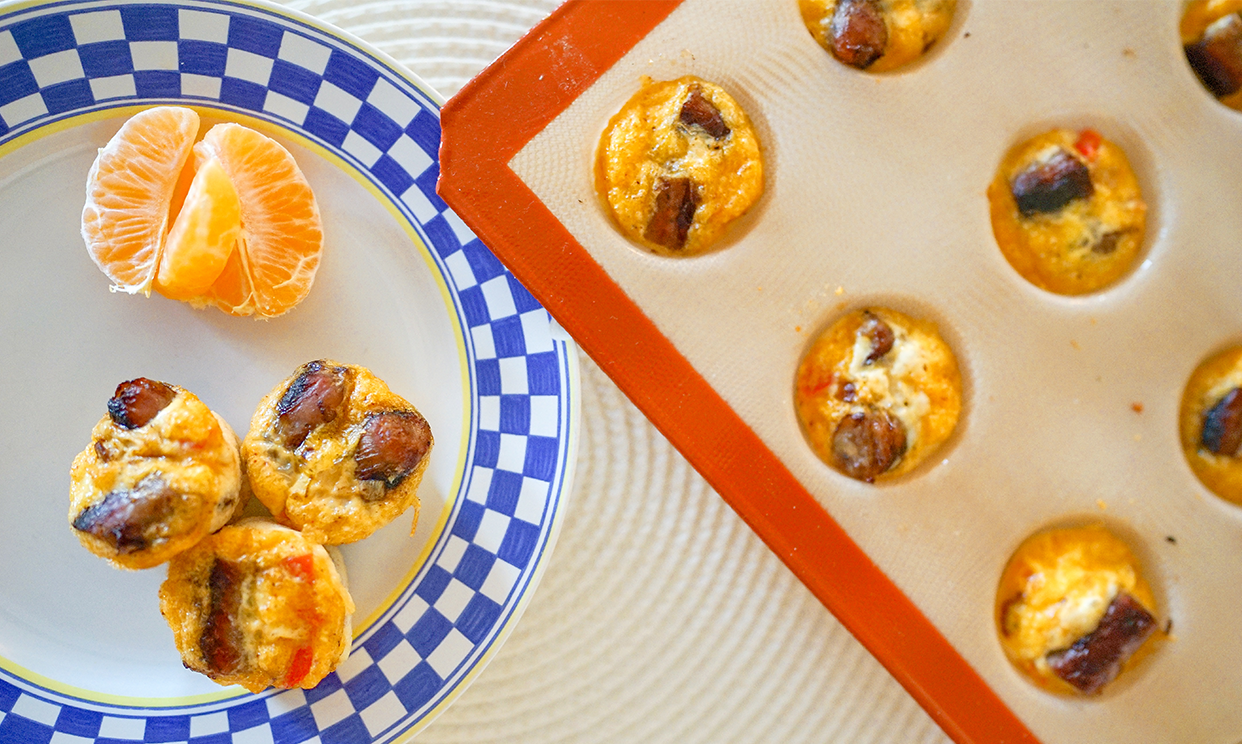 Mini sausage egg bites in a muffin tin and on a serving plate with a clementine