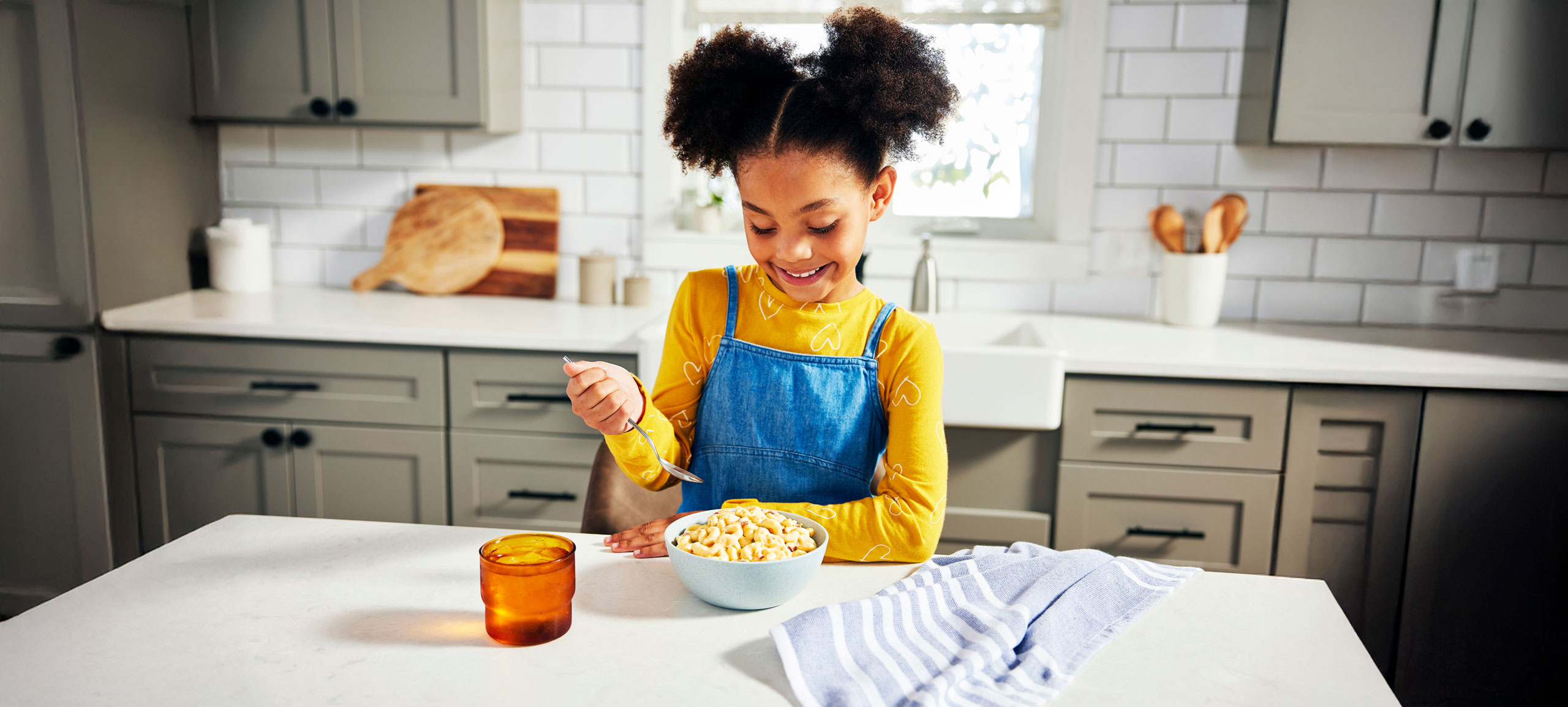 Photo of a girl in a kitchen, smiling and eating Bob Evans Macaroni and Cheese with Bacon
